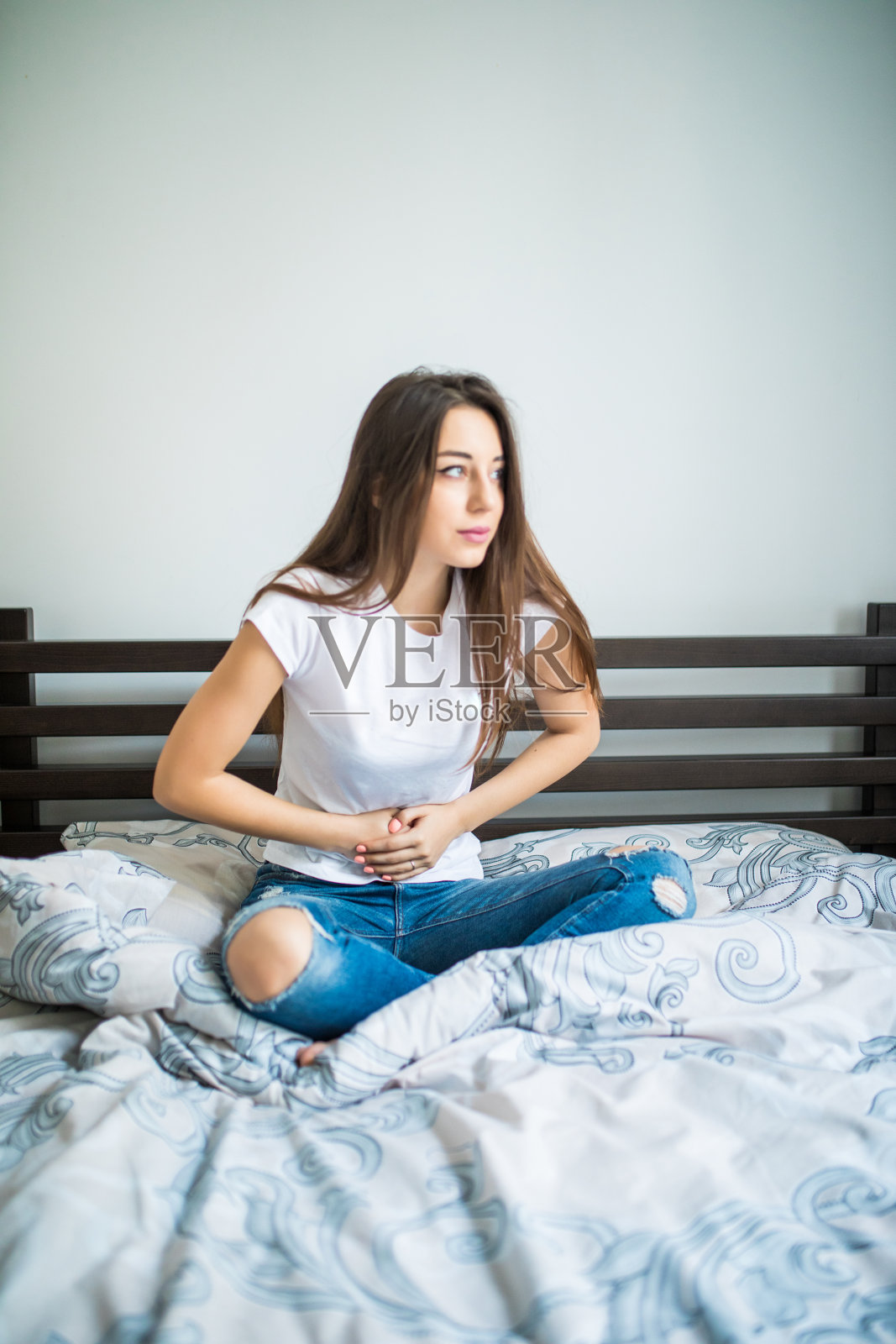 年轻美丽的女人忍受腹痛而坐在家里的床上照片摄影图片