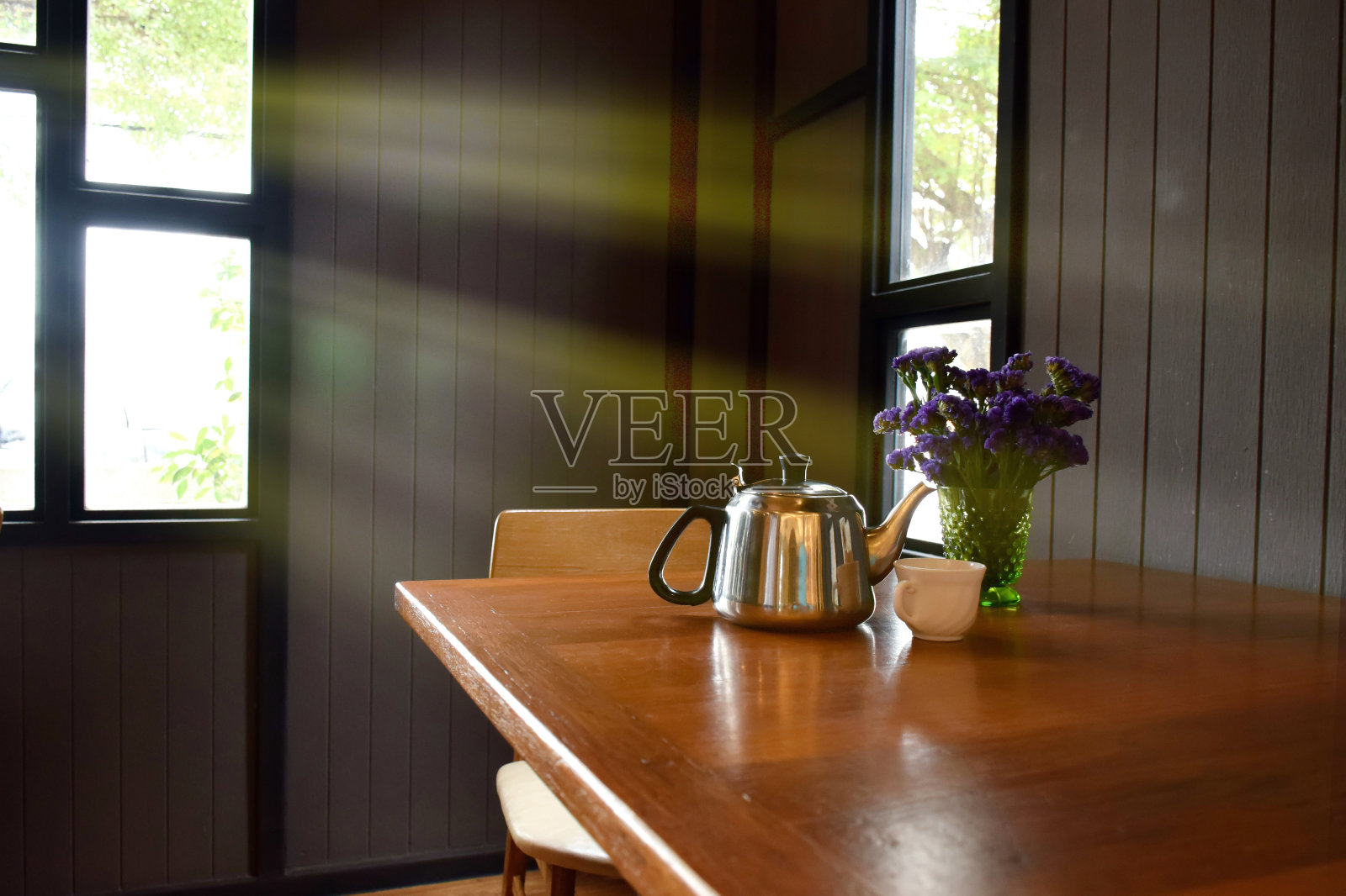 阳光透过窗户进入厨房。漂亮的木桌上放着紫色的鲜花、花瓶和茶壶。木质厨房在早晨看起来很暖和。照片摄影图片