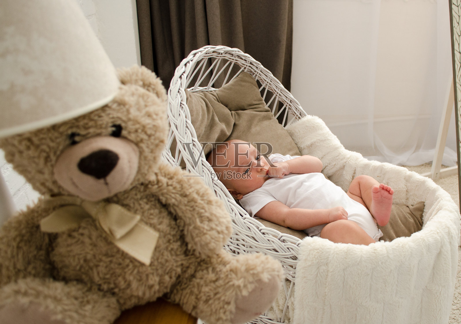 睡意朦胧的可爱宝宝躺在婴儿床或轻便床上，看着婴儿床上的移动玩具。照片摄影图片_ID:377975201-Veer图库