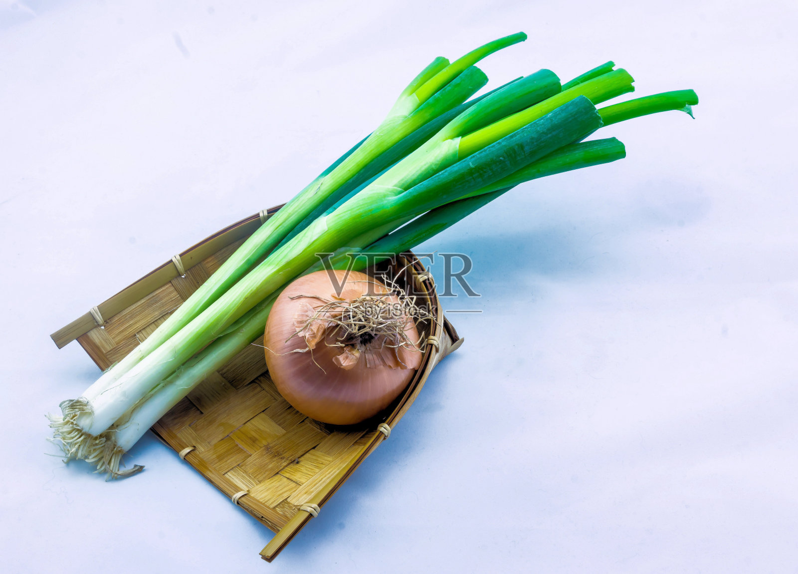韭菜和洋葱放在一个编成辫子的木盘子里照片摄影图片