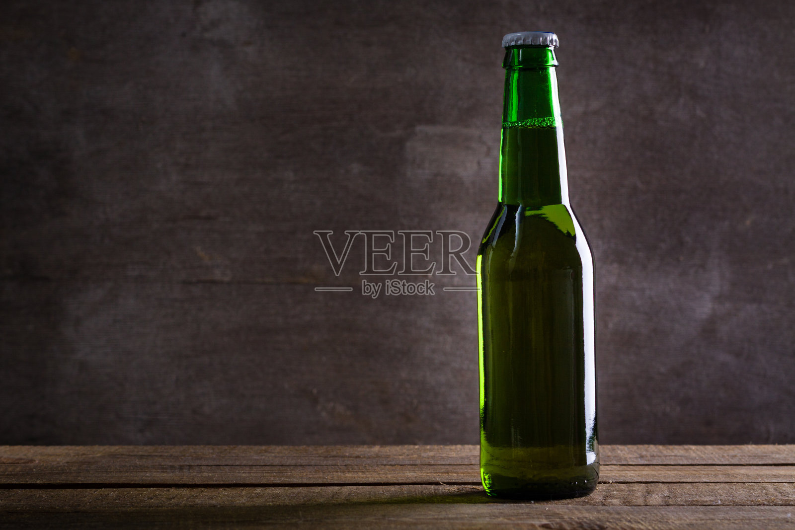 灰色的木墙上放着一瓶绿色的啤酒。照片摄影图片