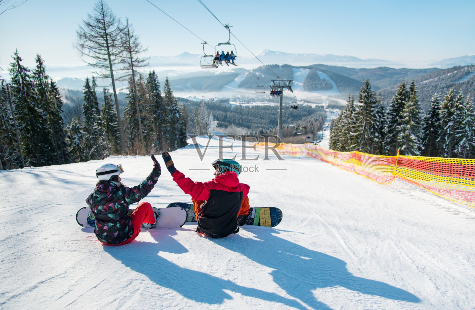 在一个阳光明媚的早晨，滑雪者们坐在滑雪缆车下的滑雪坡顶上，让我们与美丽的山脉和森林相击掌照片摄影图片
