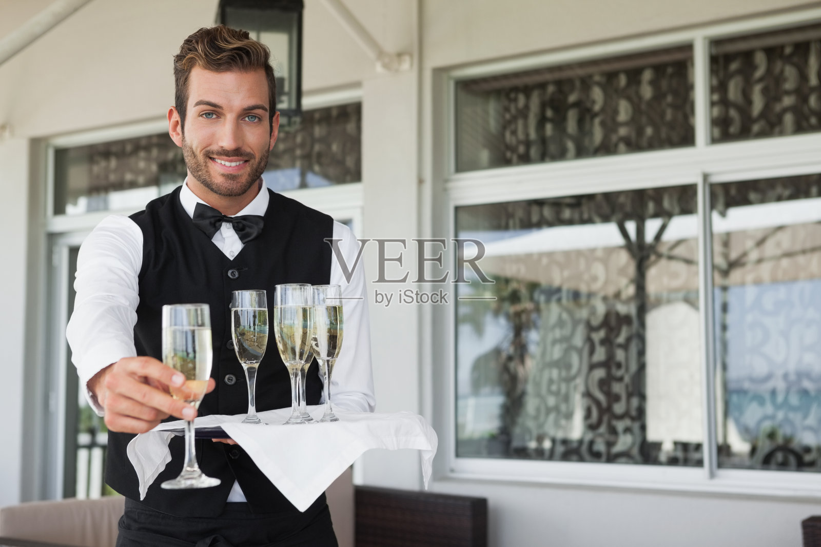 英俊的微笑服务员提供长笛的香槟照片摄影图片