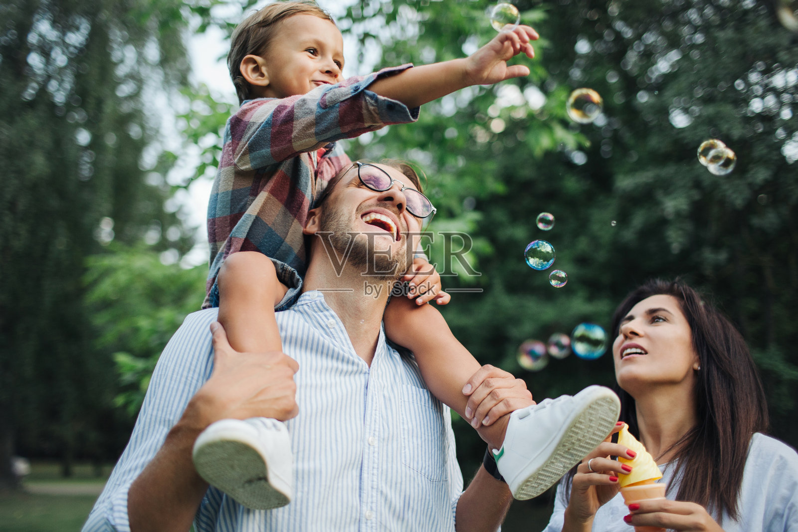 快乐的年轻家庭玩泡泡棒在公园户外照片摄影图片