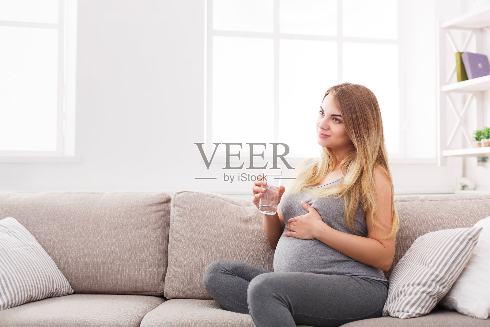 孕妇拿着一杯水坐在沙发上照片摄影图片