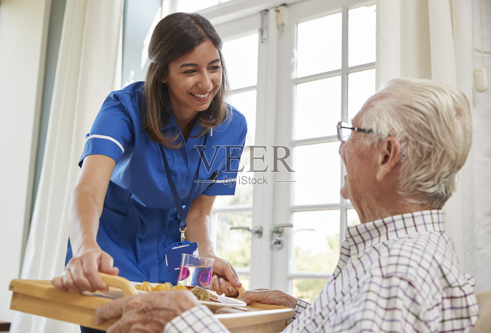 护士在为一位坐在家中扶手椅上的老人提供晚餐照片摄影图片