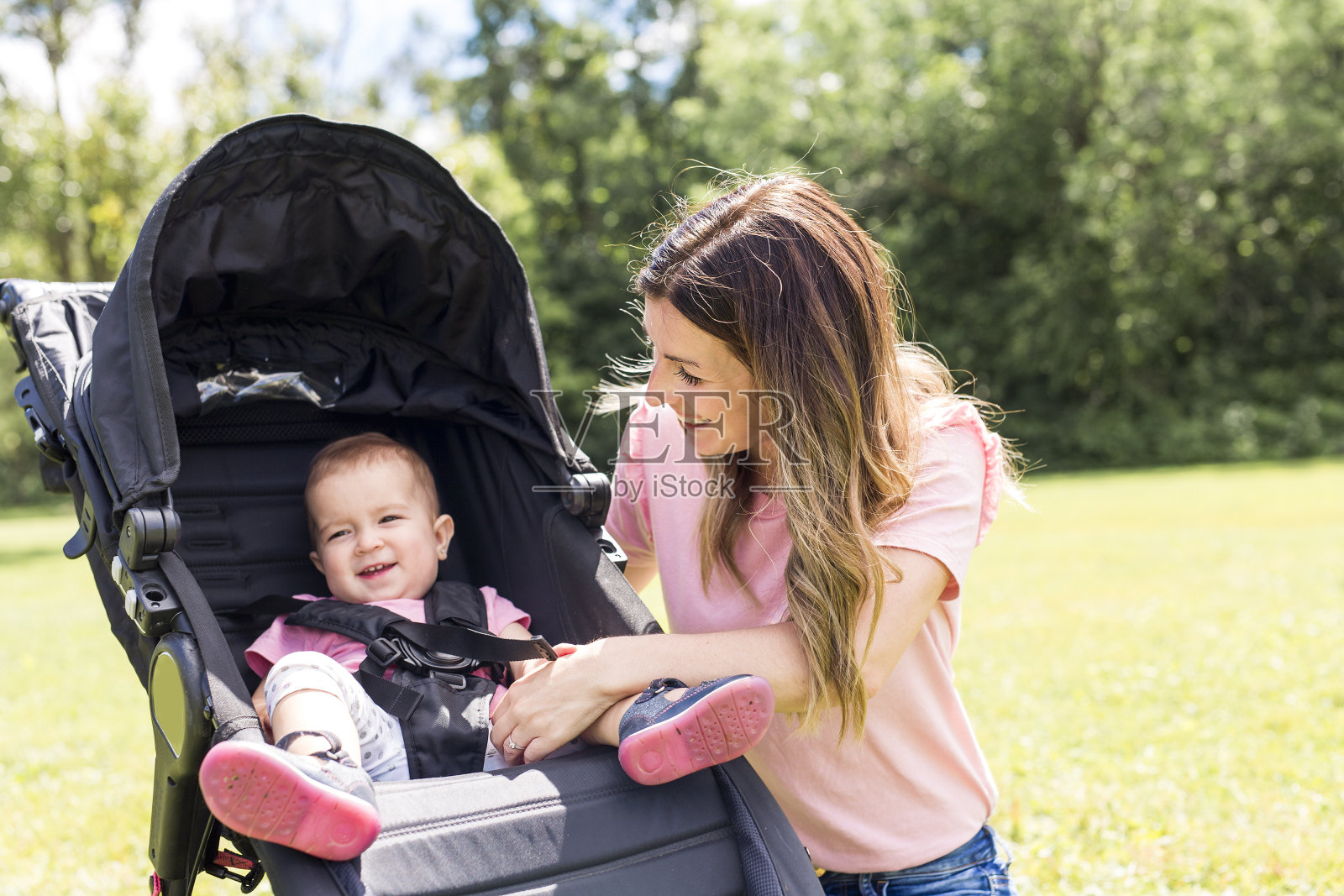 美丽的年轻女人推着婴儿车在公园里的肖像照片摄影图片