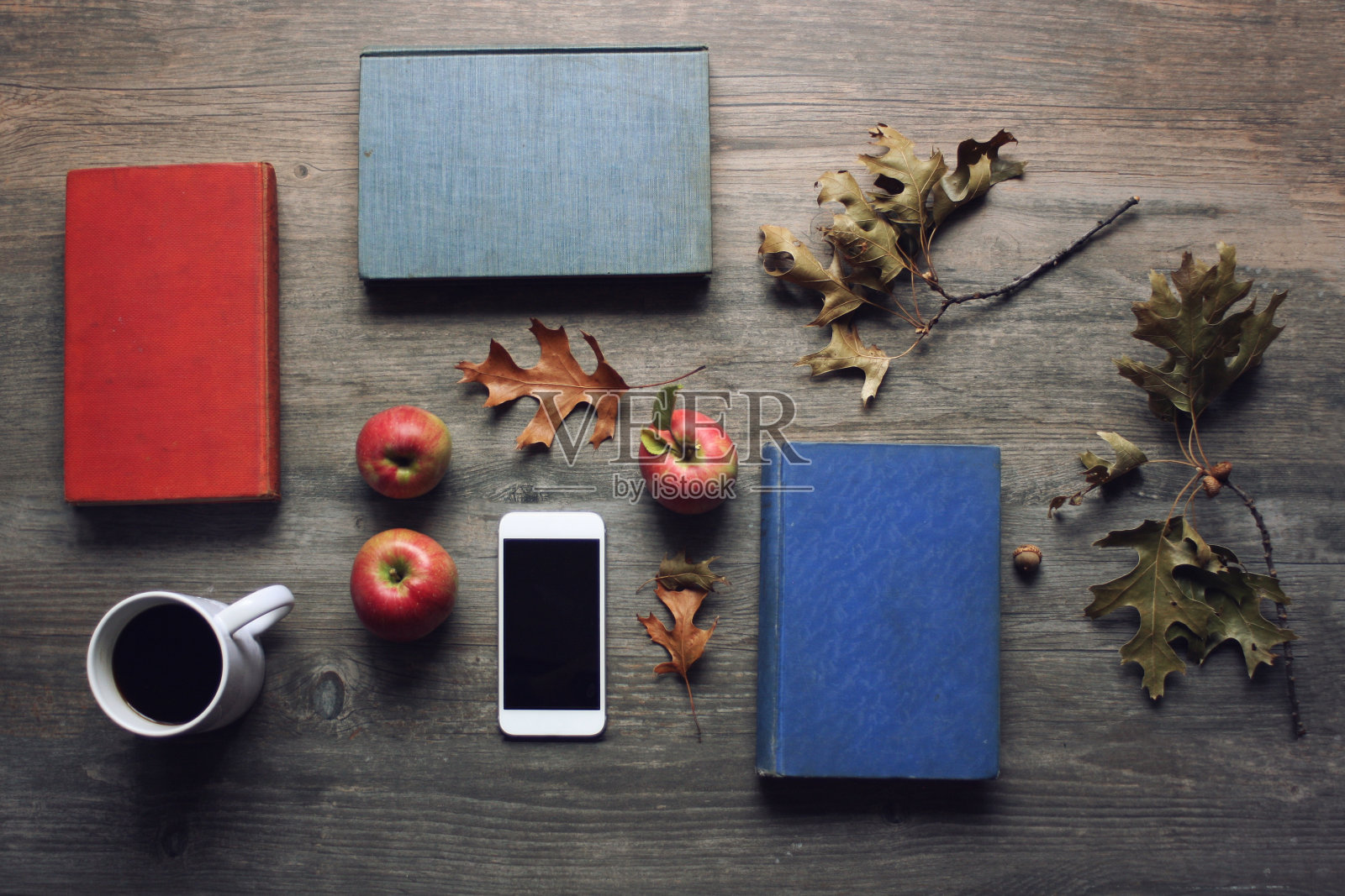 秋天的静物，红色的苹果，书籍，移动设备，黑色的咖啡杯和秋天的树叶在乡村的木制背景照片摄影图片