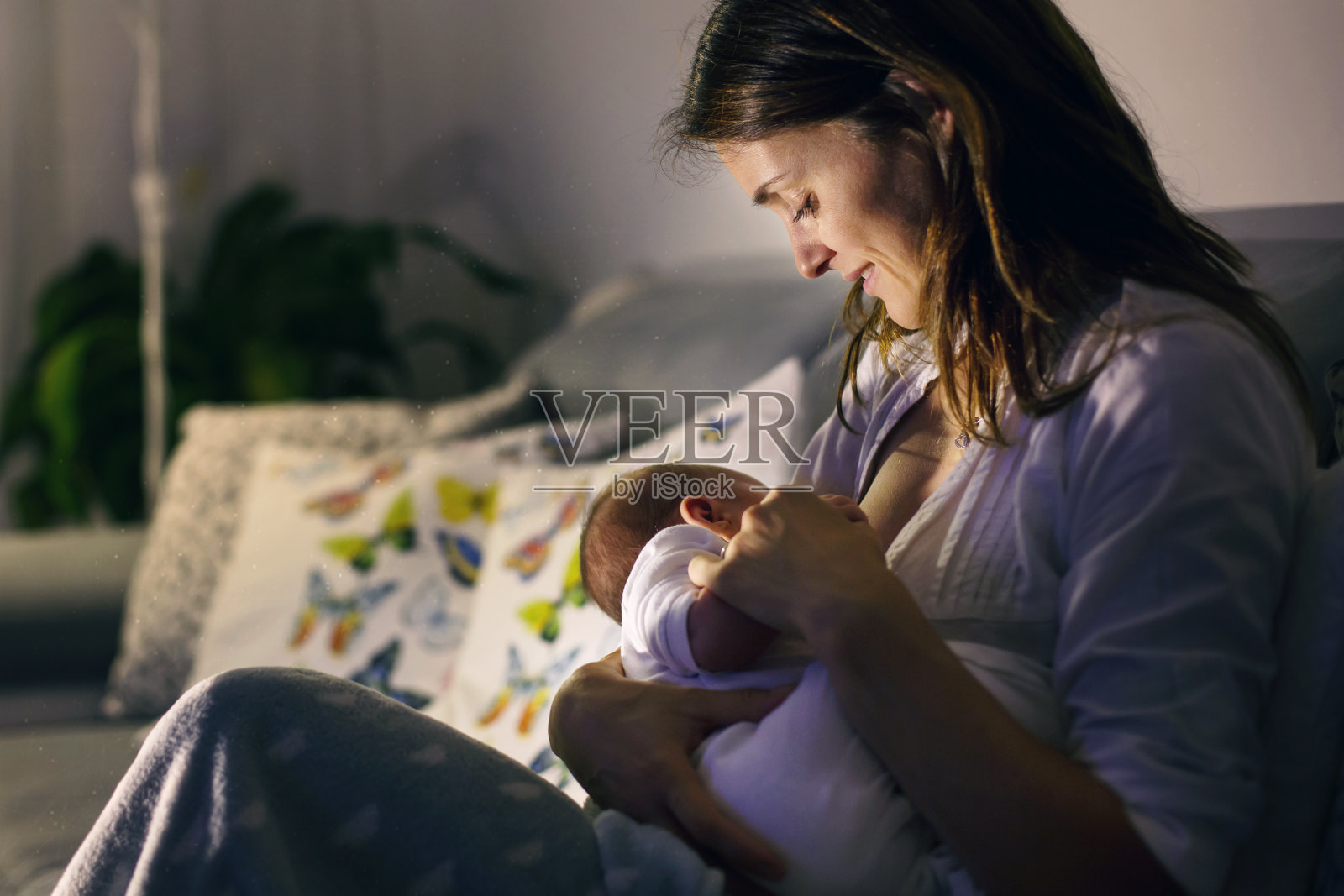 年轻漂亮的母亲，在晚上给她刚出生的儿子喂奶照片摄影图片