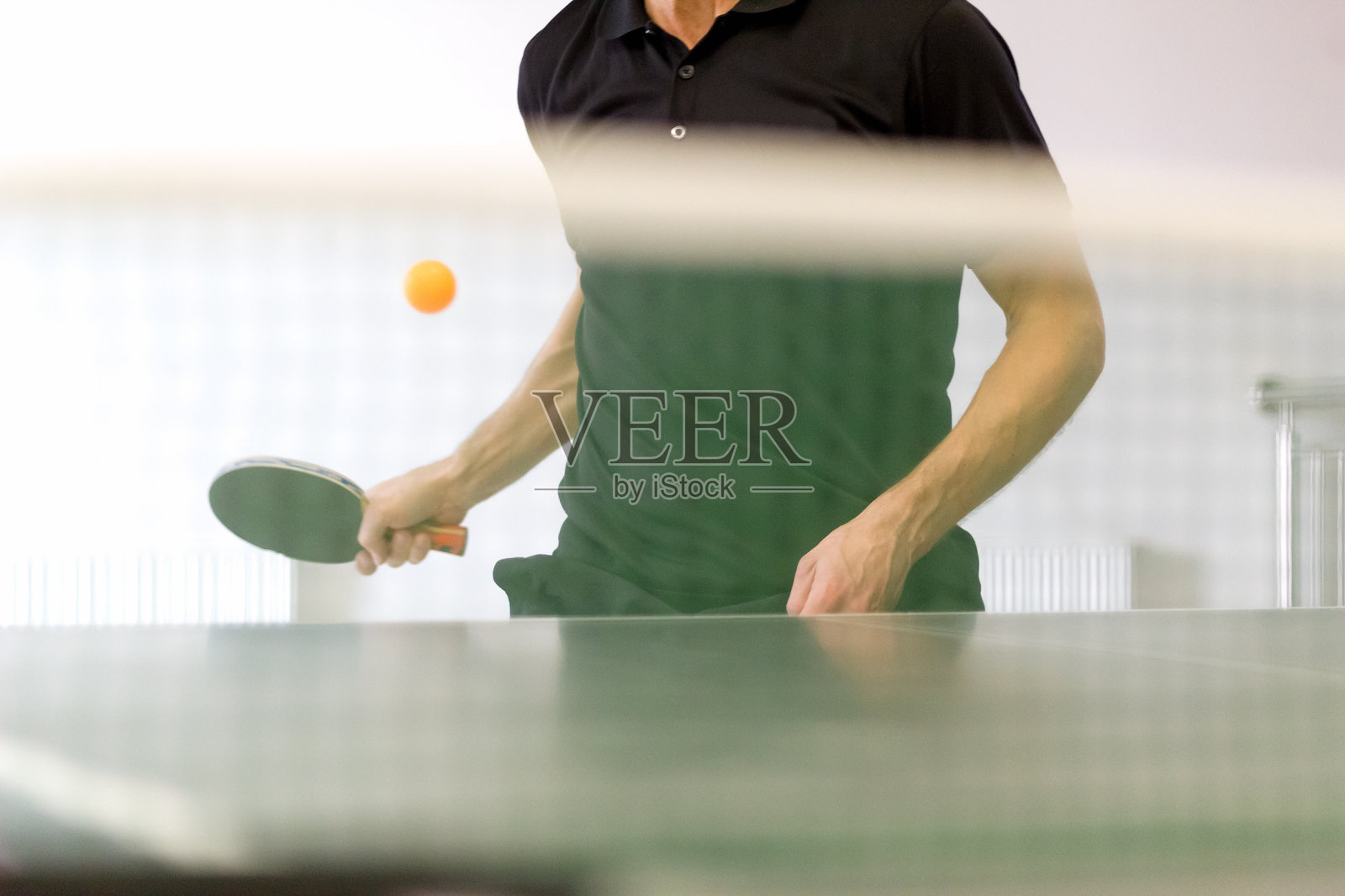 男子乒乓球运动员打正手上旋球。通过网络视图。照片摄影图片