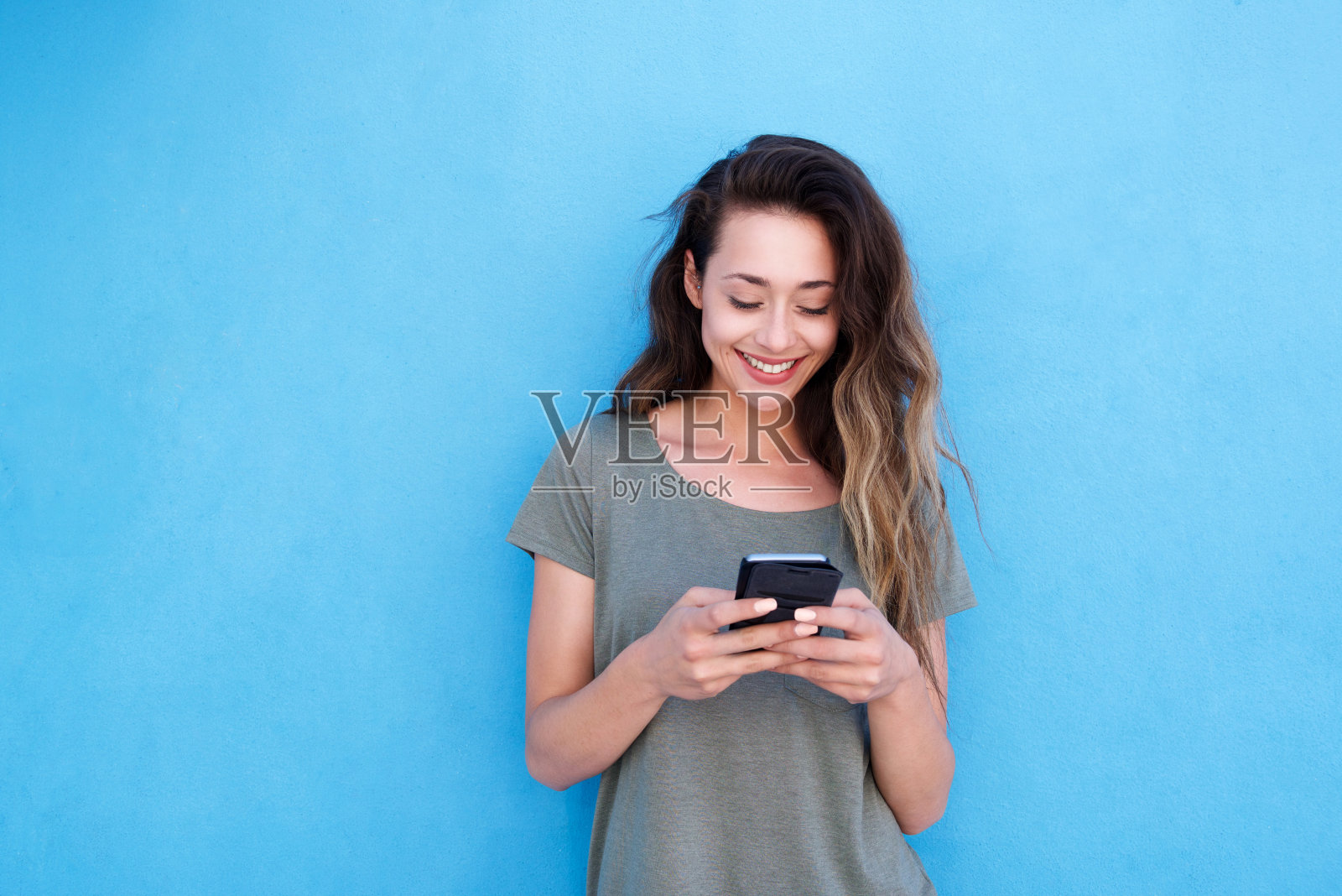 年轻微笑的女人用手机在蓝色的背景照片摄影图片
