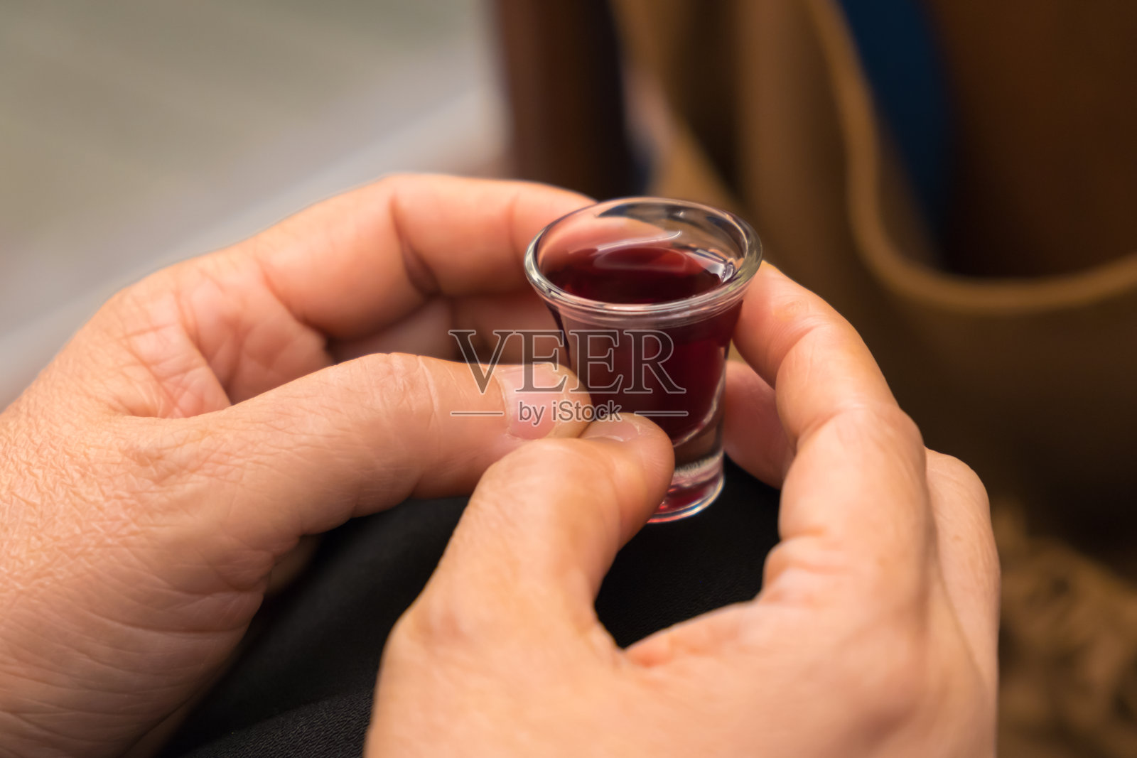 在圣餐仪式中，一位女士的手握着一个红酒杯。照片摄影图片