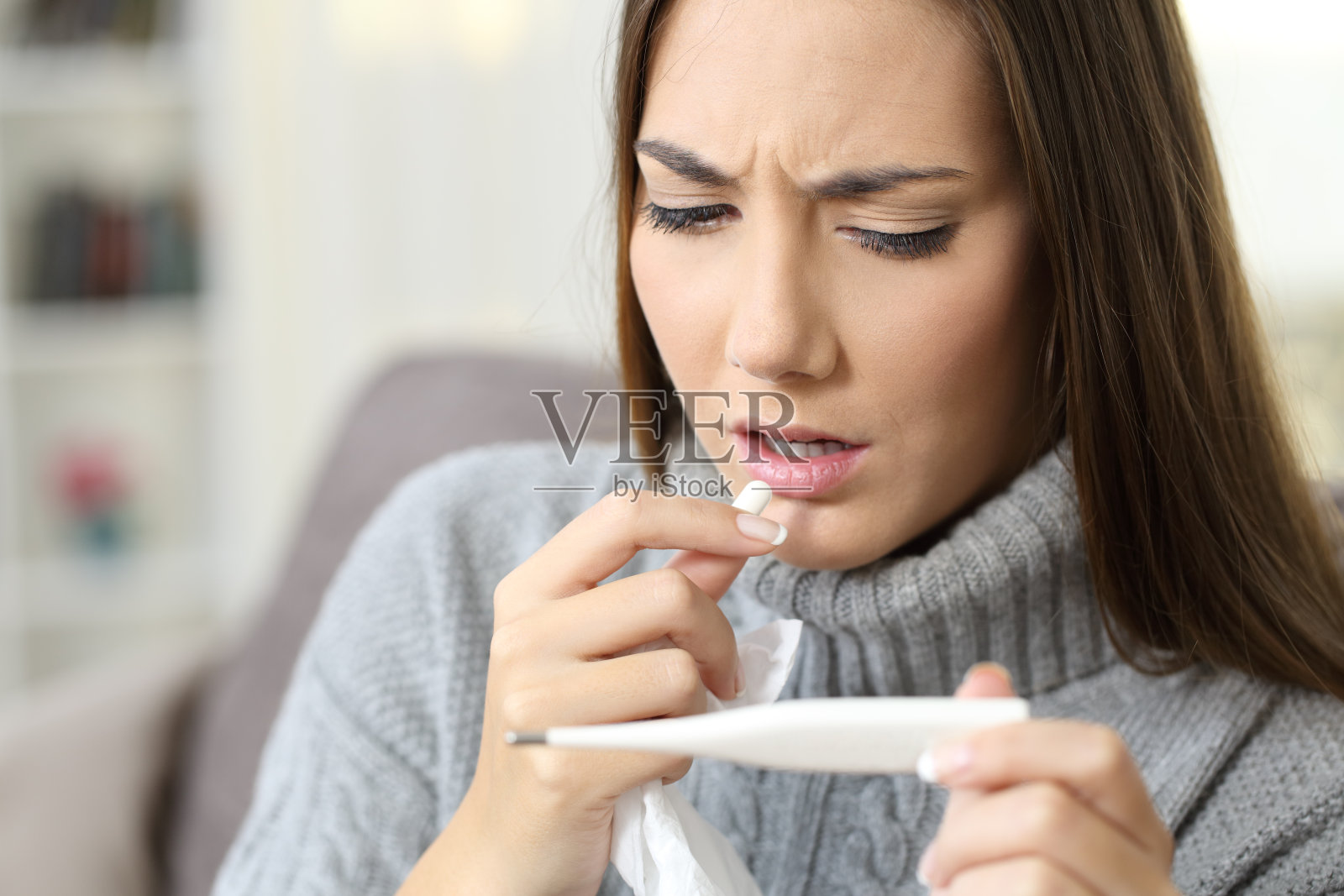 发烧的女人吃着药片，看起来像温度计照片摄影图片