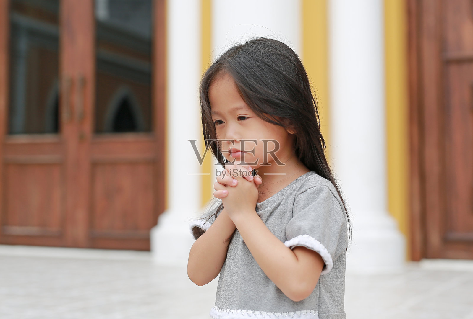 一个亚洲小女孩坐在教堂里祈祷。照片摄影图片