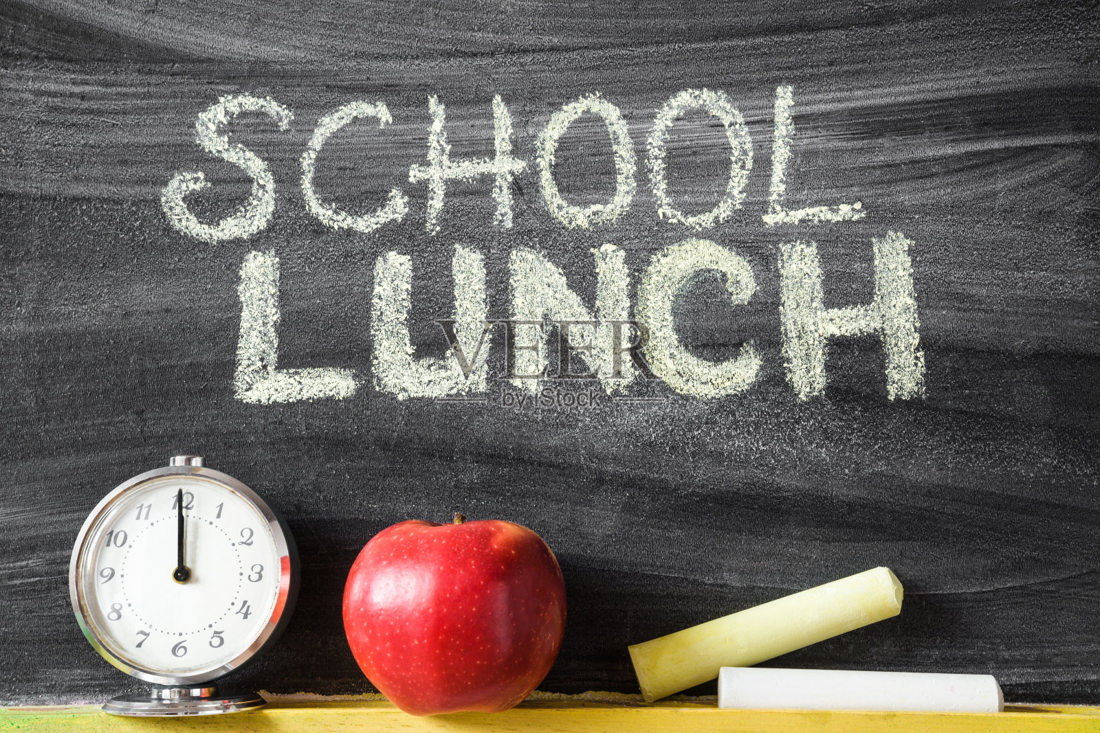 学校午餐。教室里的黑板上有粉笔、红苹果和时钟。午餐时间的概念。照片摄影图片