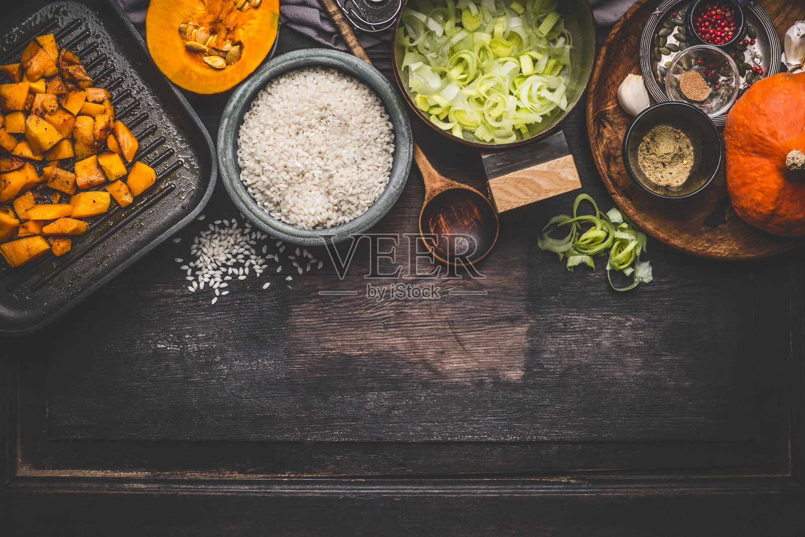 南瓜烩饭的烹饪材料在黑暗的乡村厨房的桌子上与碗，勺子和平底锅照片摄影图片