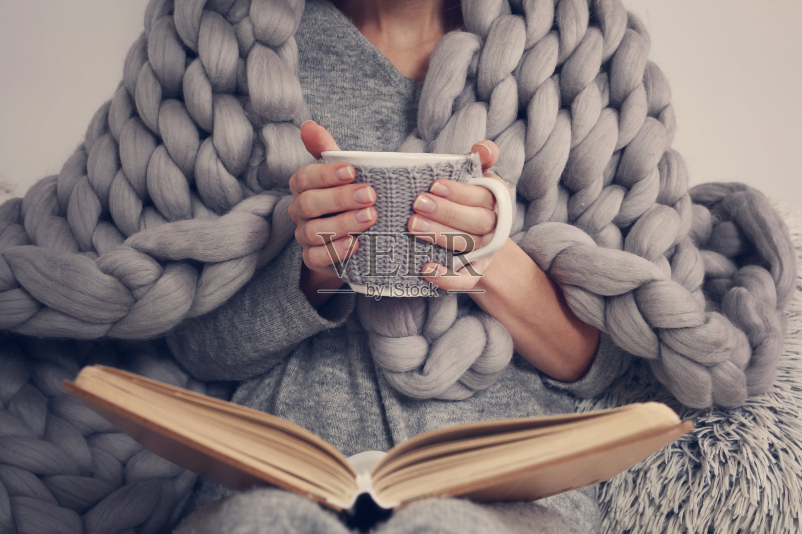 舒适的女人覆盖着温暖柔软的美利奴羊毛毯子看书。放松,舒适的生活方式。照片摄影图片
