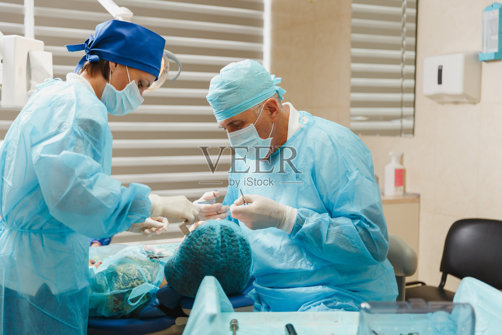 穿着制服的男老专业牙科医生和女助手在诊所灯光办公室用现代化的工具设备帮助女病人进行种植牙的操作。照片摄影图片
