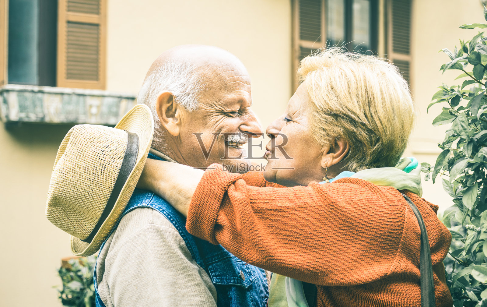 快乐的退休老两口在旅游度假的户外享受接吻的乐趣-快乐的老人和退休生活的爱的概念，男人可爱的看着妻子的眼睛-明亮的复古滤镜照片摄影图片