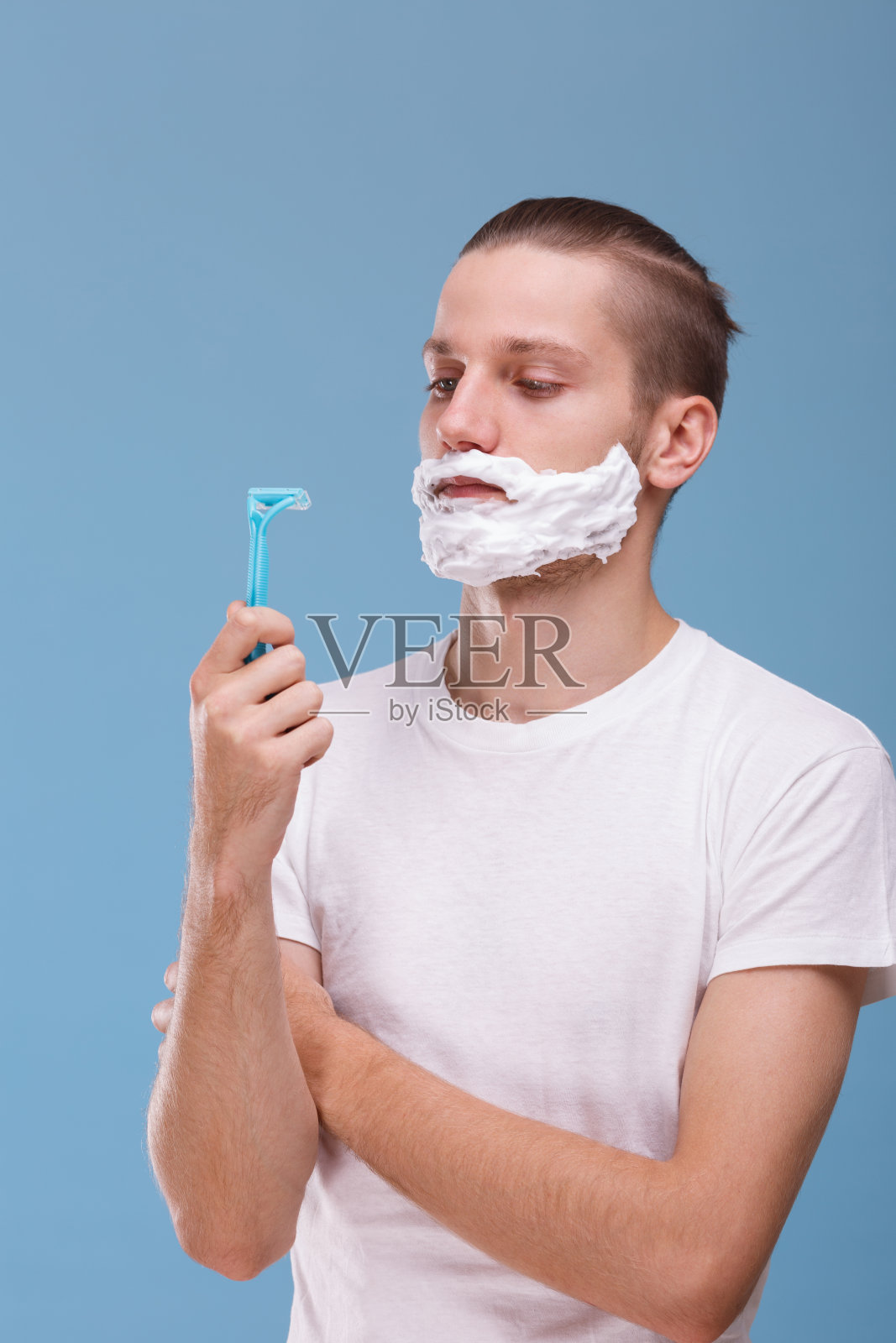 一个拿着剃须泡沫和剃刀的年轻人。卫生的概念。在蓝色背景上。照片摄影图片