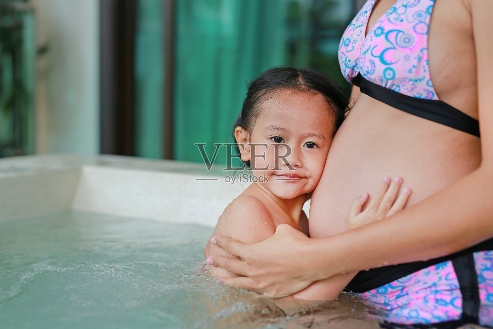 小女孩在浴缸里听着孕妇的肚子。照片摄影图片