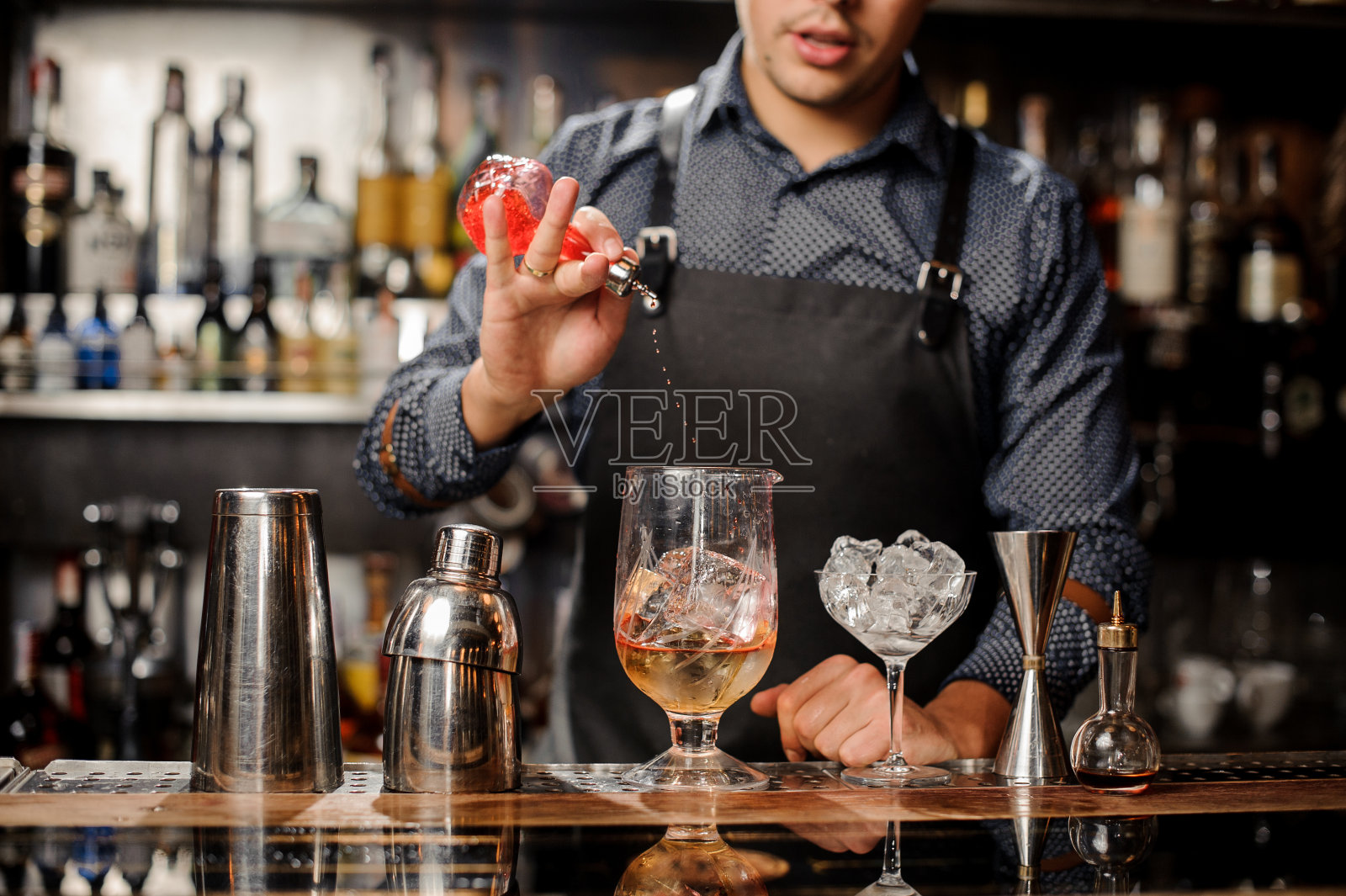 调酒师将糖浆倒入加冰的鸡尾酒杯中照片摄影图片