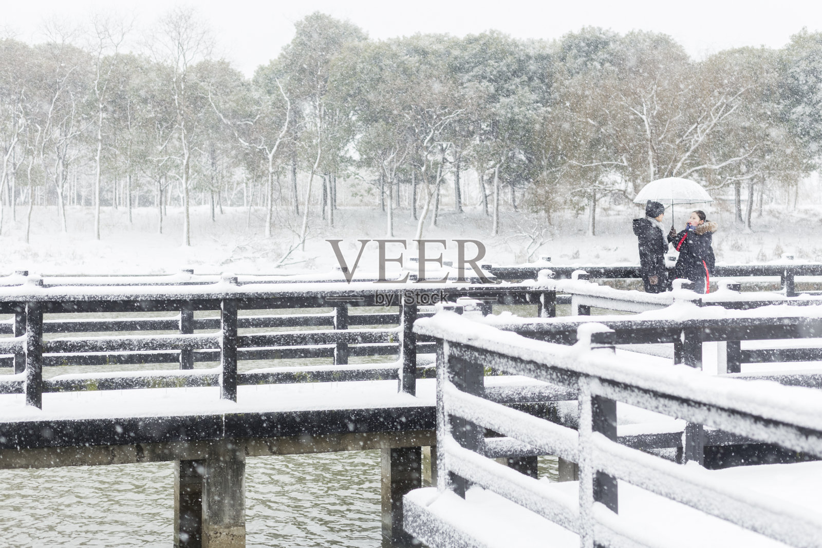 一对情侣撑着伞站在白雪覆盖的木桥上照片摄影图片