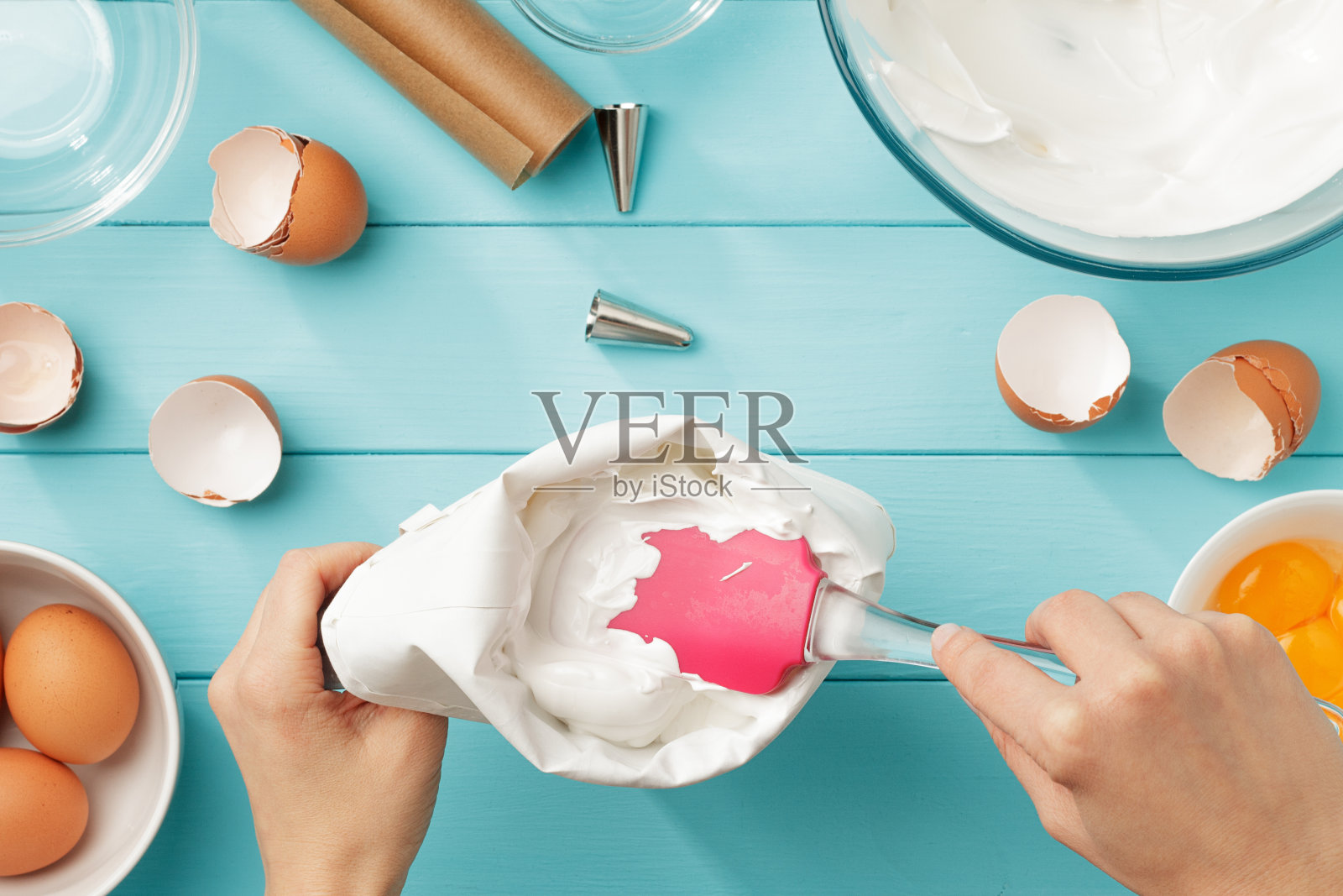 女性的手填充糖果袋与打发蛋白奶油在蓝色木制背景。照片摄影图片