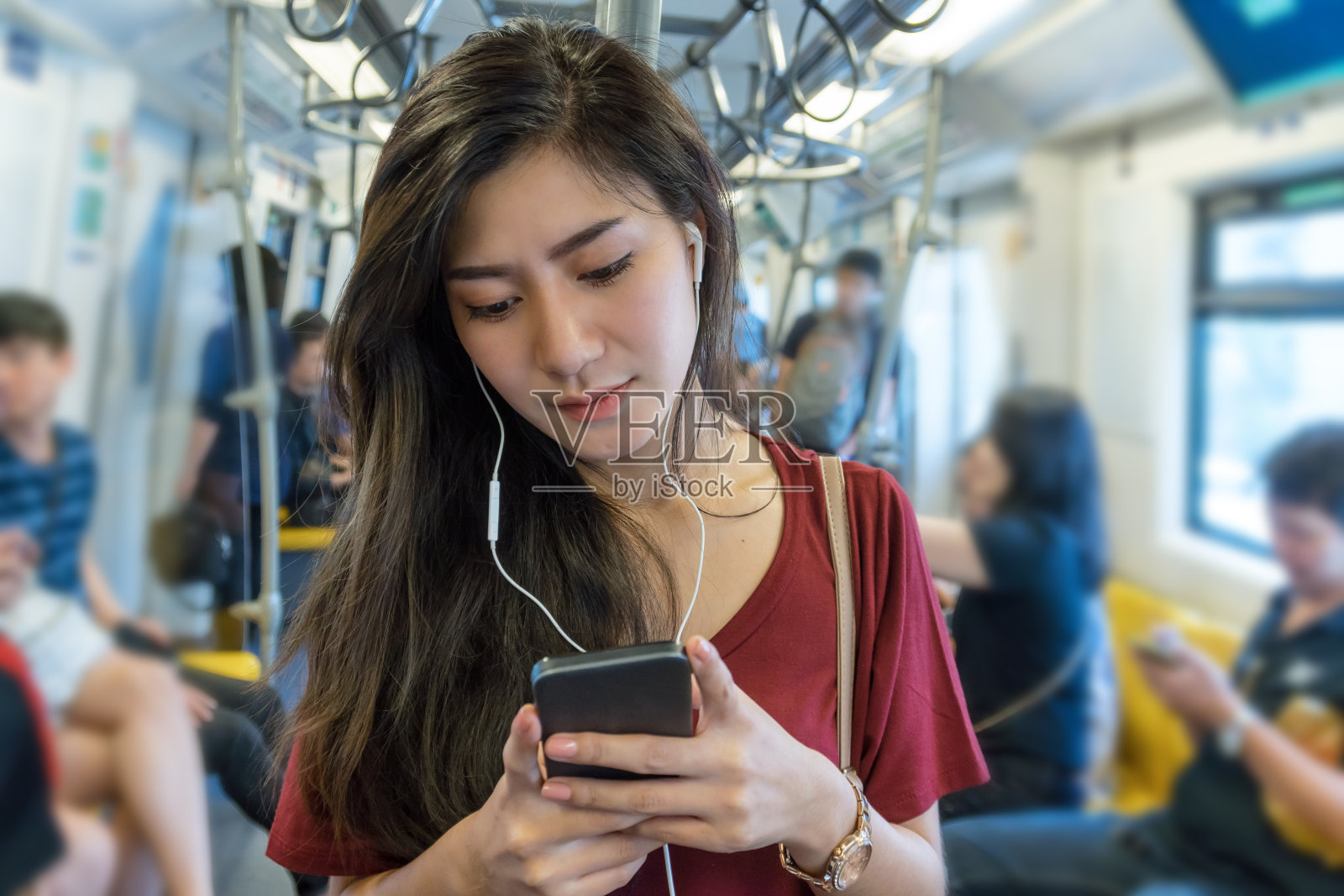 亚洲女性乘客穿休闲装使用和听歌曲通过智能手机在轻轨或地铁在大城市旅行，生活方式和交通理念照片摄影图片