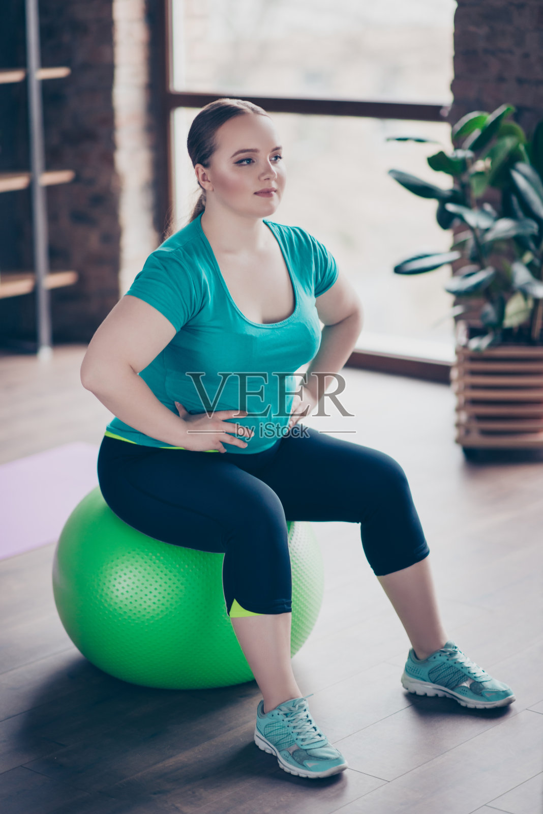 垂直全身全尺寸照片，欢快自信集中年轻胖胖女人穿着运动服，她正在用绿色的fitball锻炼，看着她的教练照片摄影图片