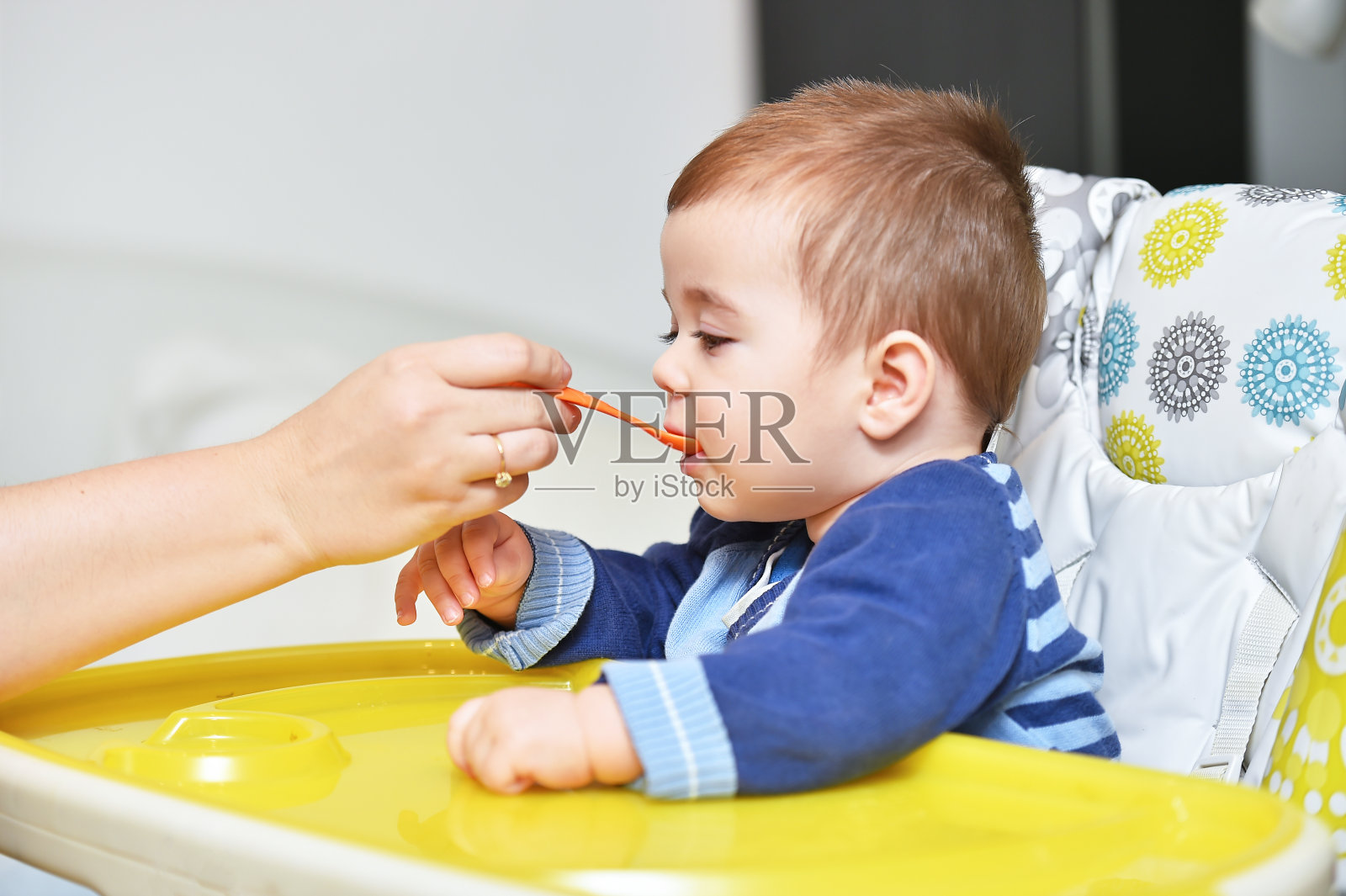 坐在婴儿椅上的小男孩用勺子吃饭照片摄影图片