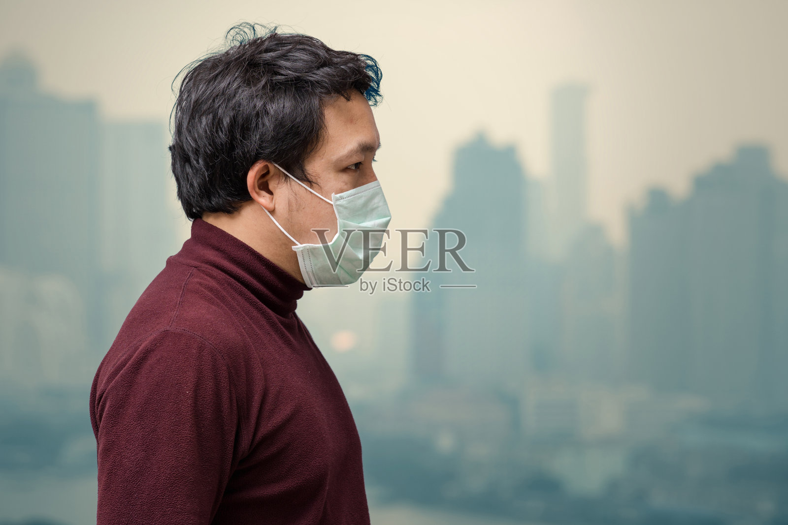 亚洲男子戴着口罩在高公寓的阳台上防止空气污染，可以看到污染和浓雾笼罩曼谷城市景观背景，保健概念照片摄影图片