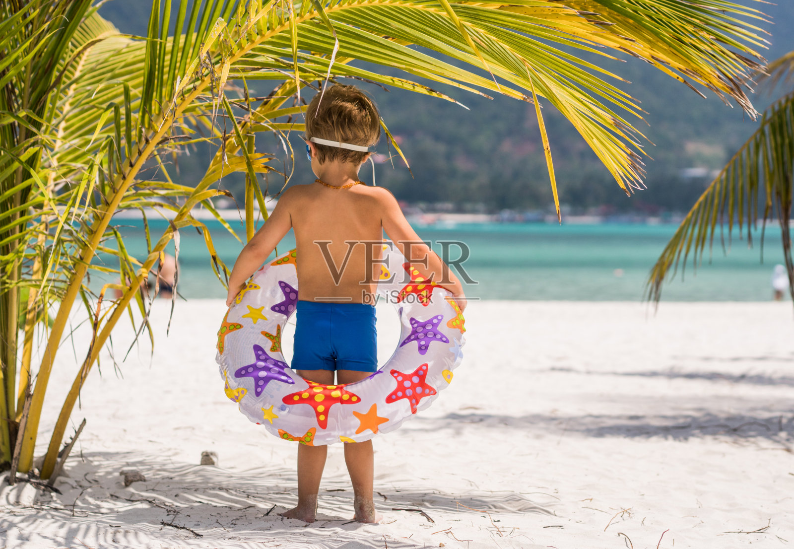 一个男孩的背影与游泳管在阴凉的海滩。照片摄影图片