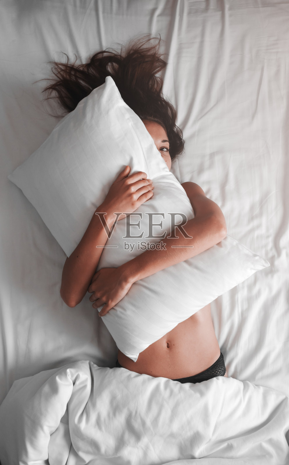 美丽性感的年轻女子覆盖在枕头上，而躺在床上照片摄影图片