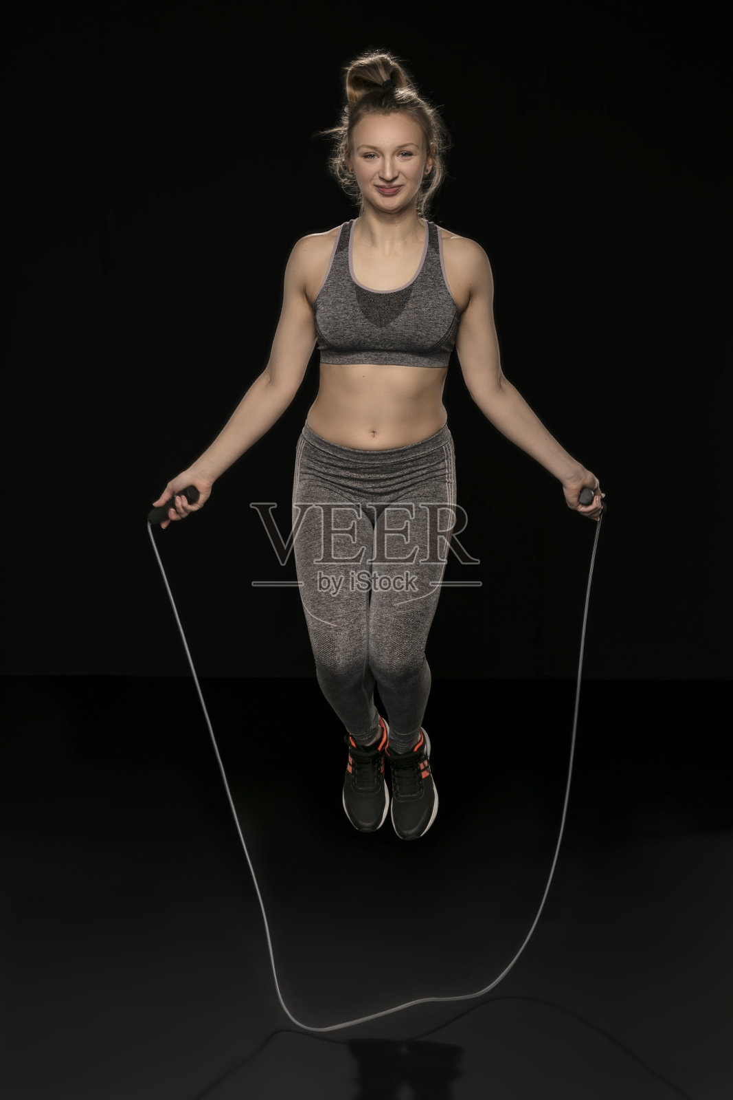 美丽的运动女孩正在练习跳绳，孤立在黑色的背景照片摄影图片