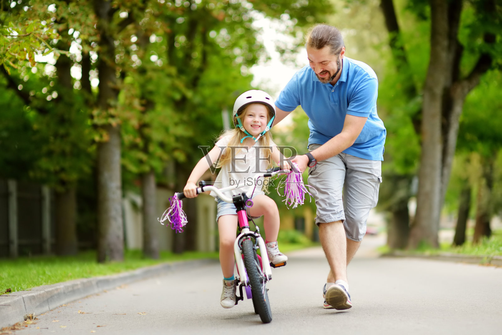 快乐的父亲教他的小女儿骑自行车。学骑自行车的孩子。照片摄影图片