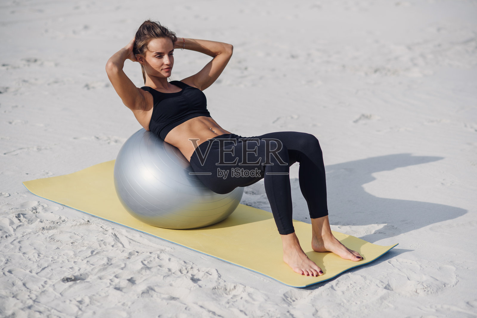 运动和健康的生活方式概念。美丽的健身女孩做腹部运动与健身球在海滩上。照片摄影图片