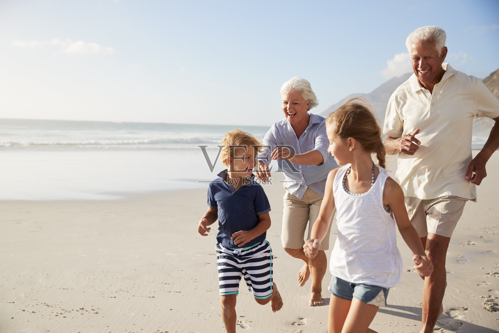 暑假里，祖父母和孙辈们在海滩上跑步照片摄影图片