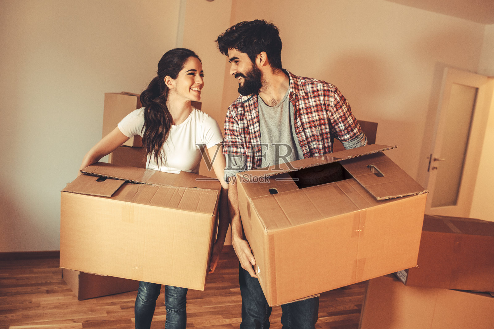 一对年轻夫妇带着大纸板搬进新家。移动的房子。房地产的概念。照片摄影图片