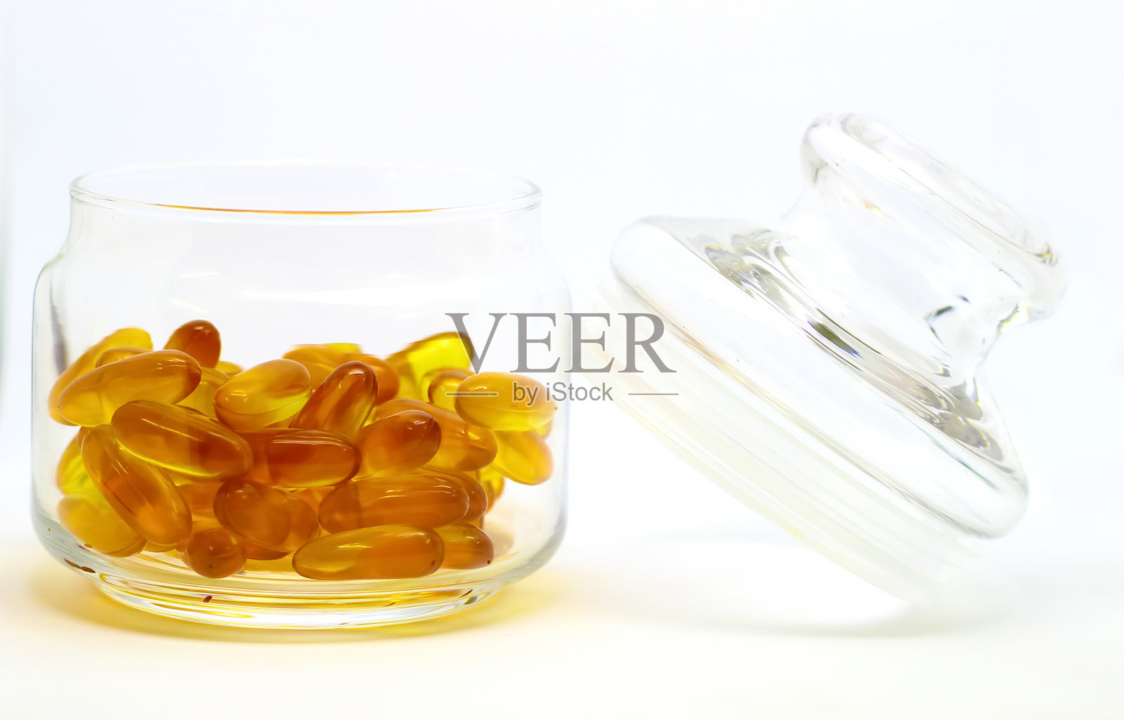 鱼肝油- 3维生素e凝胶胶囊隔离在白色背景的透明玻璃瓶盖上照片摄影图片