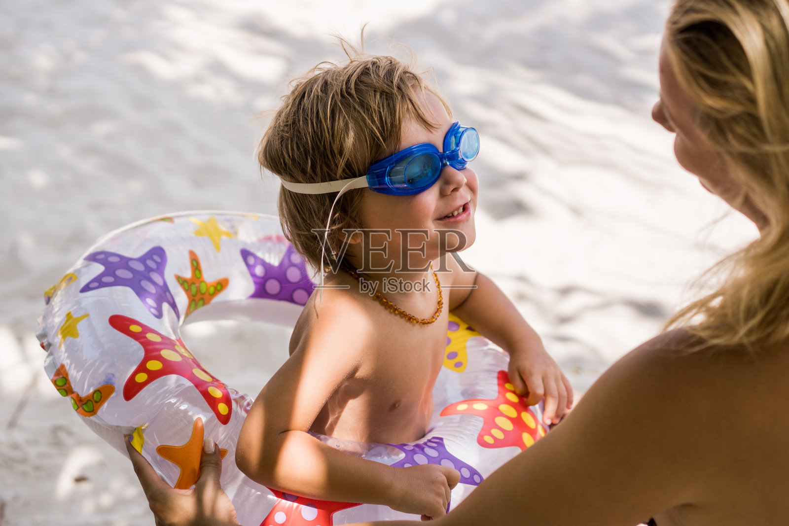 可爱的小男孩拿着游泳器材在海滩上和妈妈说话。照片摄影图片