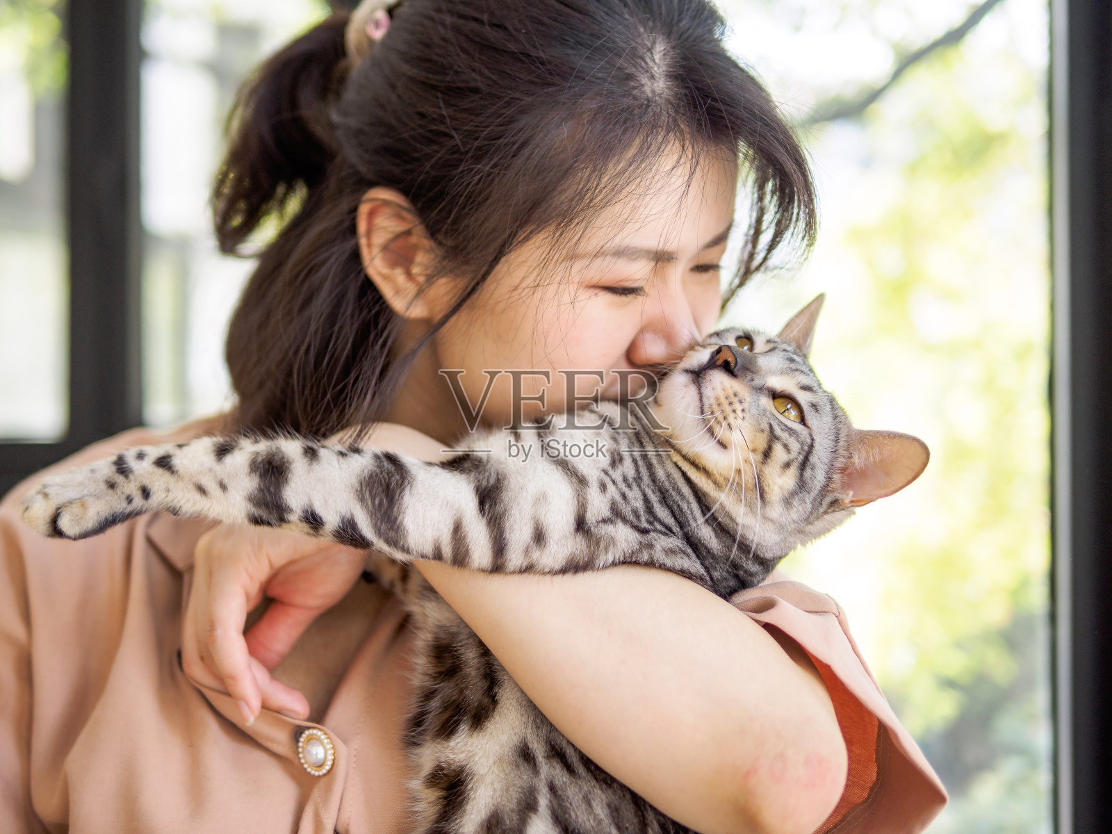 一个美丽的年轻中国女孩抱着一只孟加拉猫，亲吻猫的脖子，专注于猫的眼睛，充满爱，宠物爱人的概念。照片摄影图片