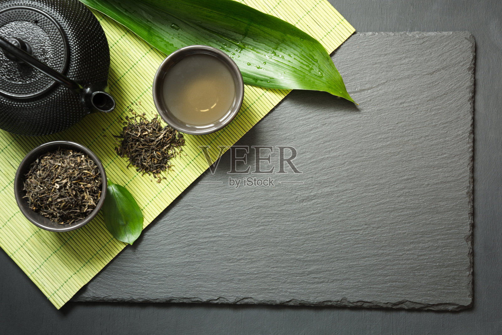 黑石板背景上的日本绿茶。黑色茶壶和碗与绿茶。顶部视图与复制空间。照片摄影图片