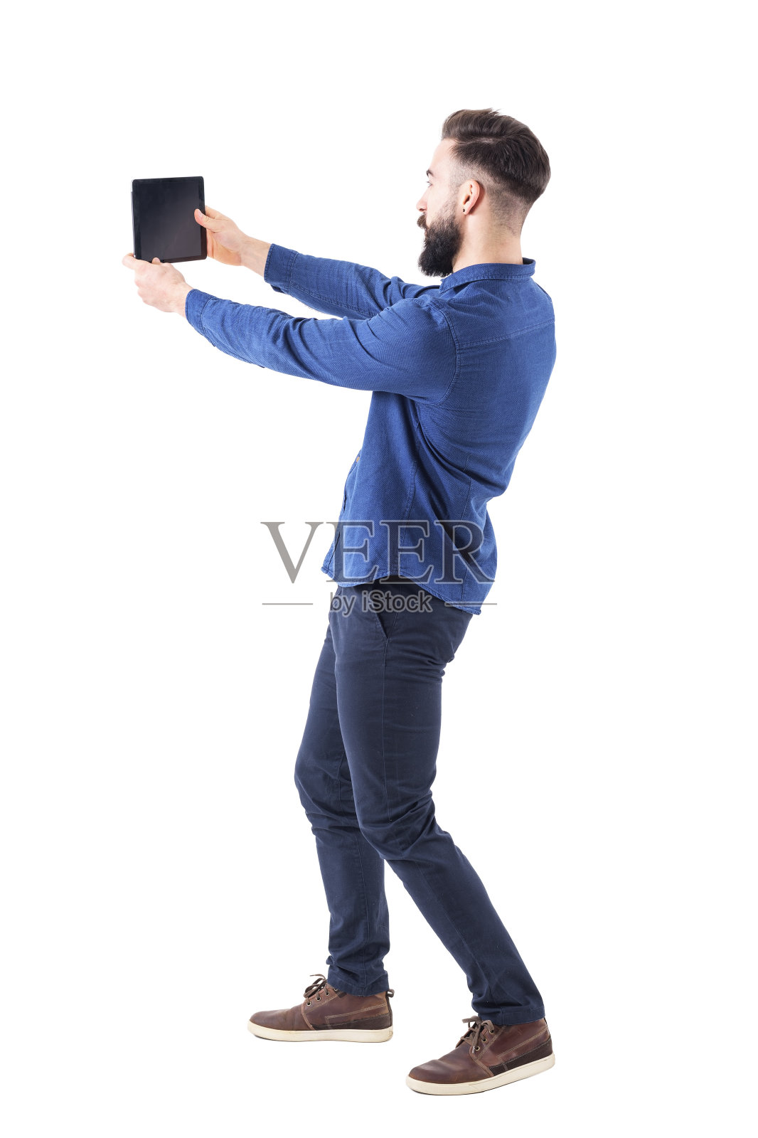 留胡子的年轻人用平板电脑或大手机自拍。侧视图照片摄影图片