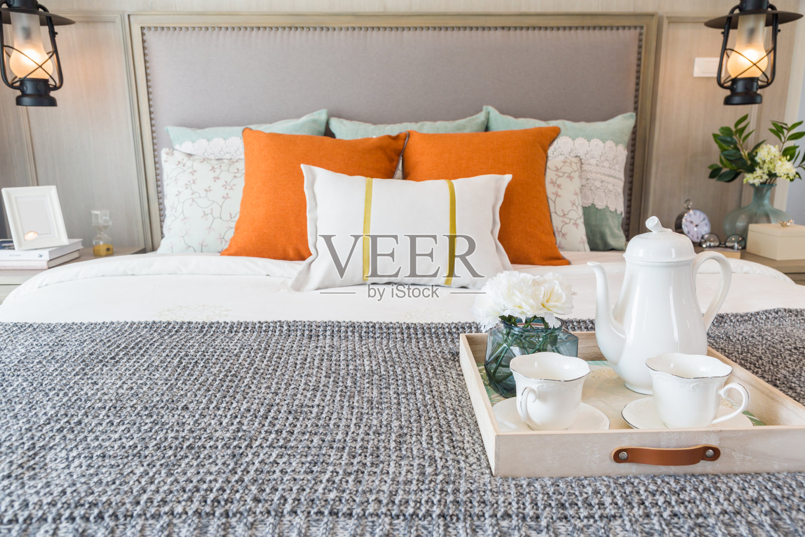 许多枕头和豪华茶具放在灰色的毯子上，配有复古床头灯、框架和植物。照片摄影图片