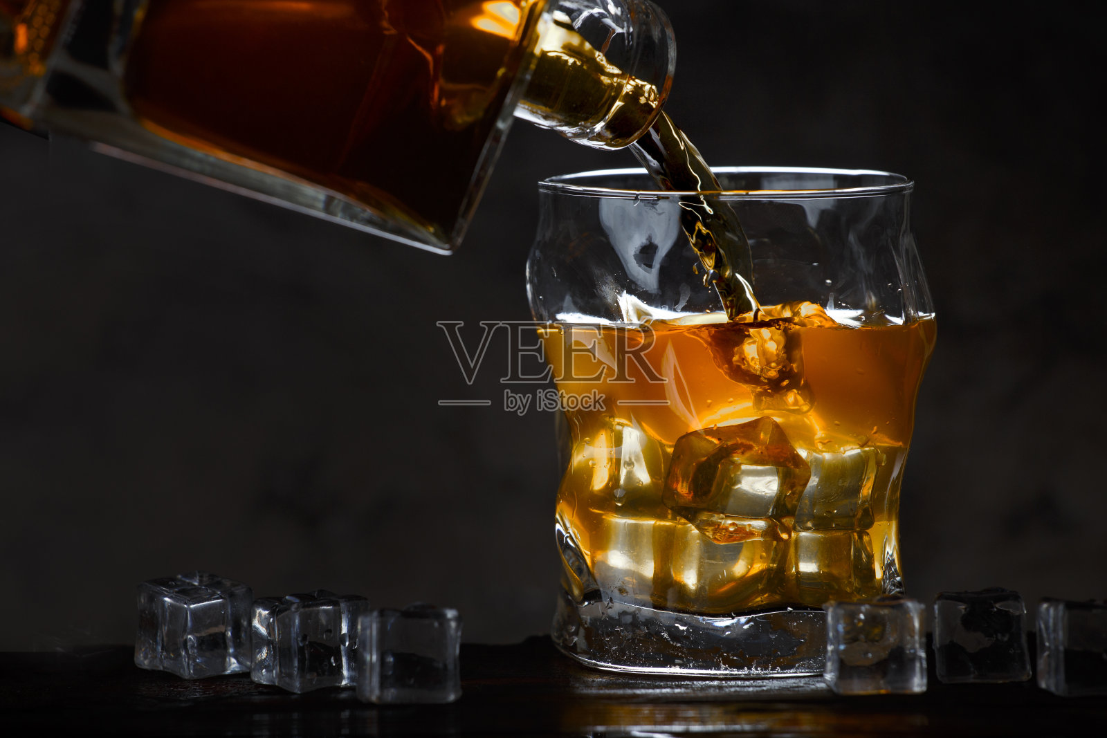 威士忌酒瓶在黑暗的背景下流入一杯冰照片摄影图片