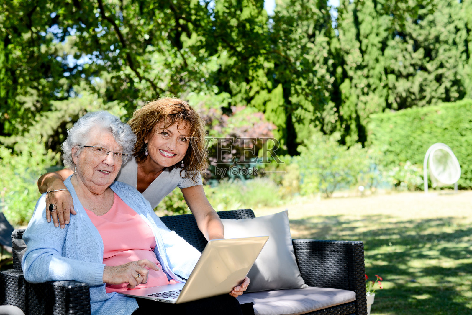 开朗成熟的女人与母亲，年长的老年女性坐在户外和玩笔记本电脑在退休之家医院的花园照片摄影图片