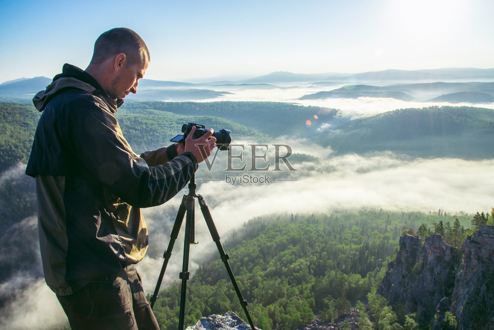摄影师用三脚架在落基山峰上拍摄照片。美丽的薄雾日出和山谷观云。照片摄影图片