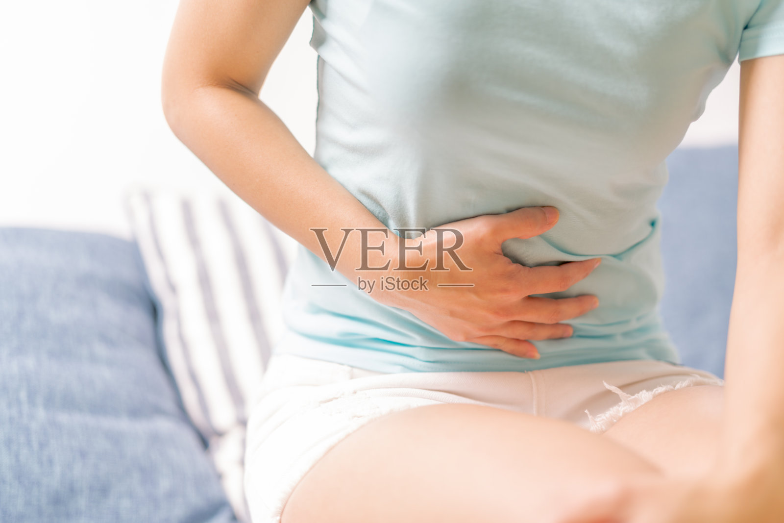 年轻女子坐在沙发上腹痛，胃疼，是经前综合症的症状照片摄影图片