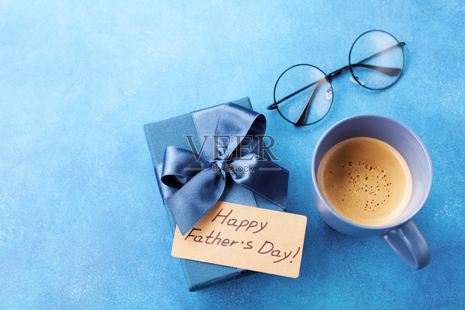 在父亲节快乐的早餐上，蓝色桌子上放着一杯咖啡，一个礼盒和一副眼镜。照片摄影图片